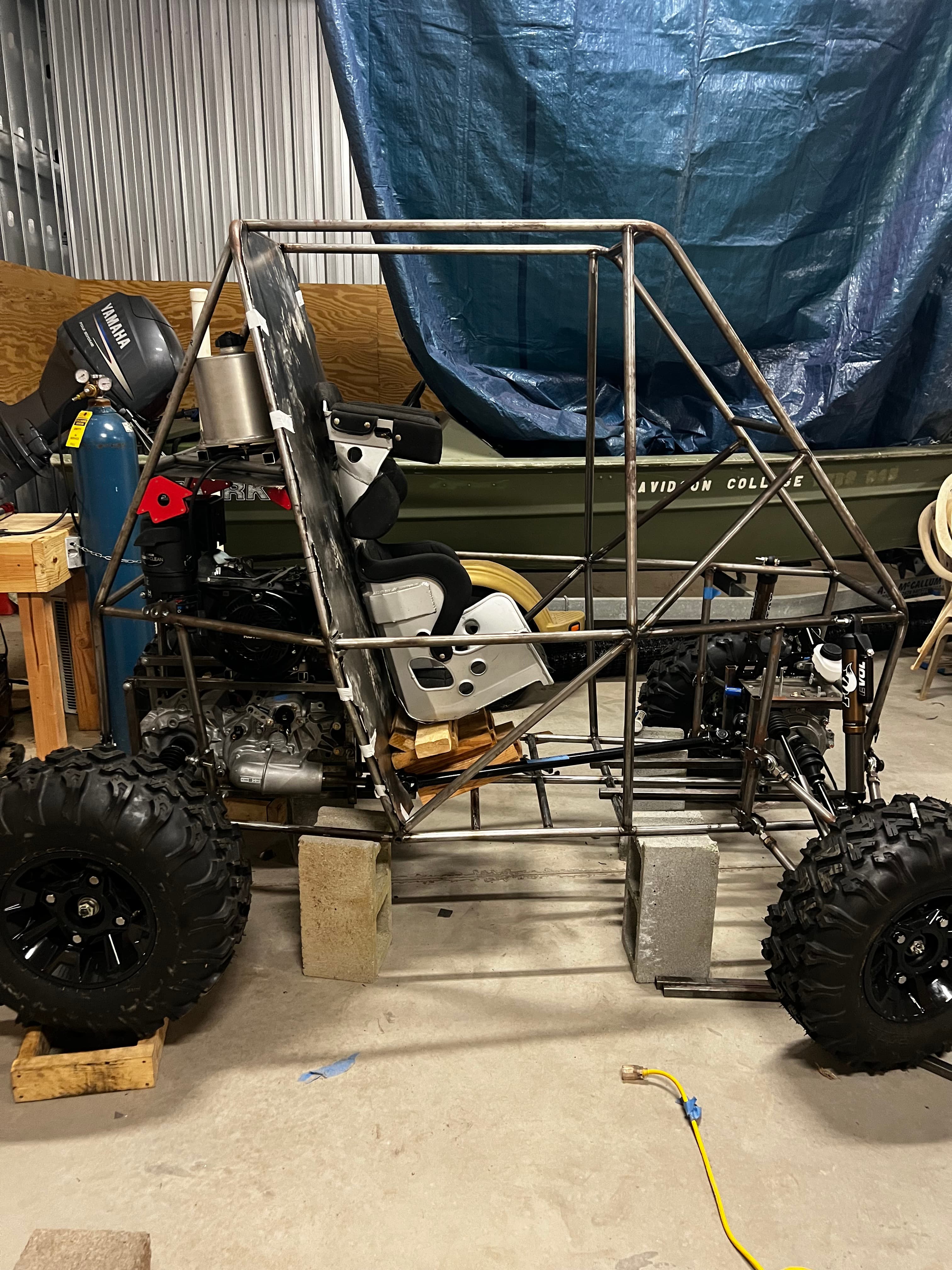 Side profile of vehicle with engine mounted, wheels on, seat visible, and welder next to it
